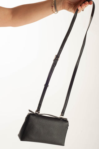 A black pebbled leather shoulder bag with a long adjustable strap, held by a person's hand against a plain white background.