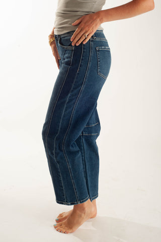 A person wearing dark blue cropped jeans with a relaxed straight-leg fit, shown from the waist down against a plain white studio background.