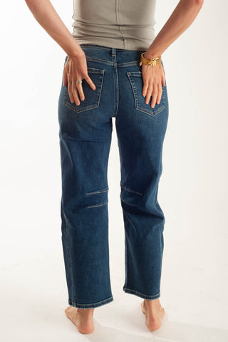 A person shown from the back wearing dark blue straight-leg jeans, standing barefoot against a plain white studio background.