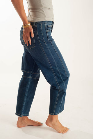 A person wearing loose-fitting dark blue denim jeans with contrast stitching, shown from the waist down against a plain white studio background.
