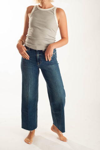 A model wearing a light beige ribbed tank top and dark blue wide-leg cropped jeans, standing barefoot against a plain white studio background.