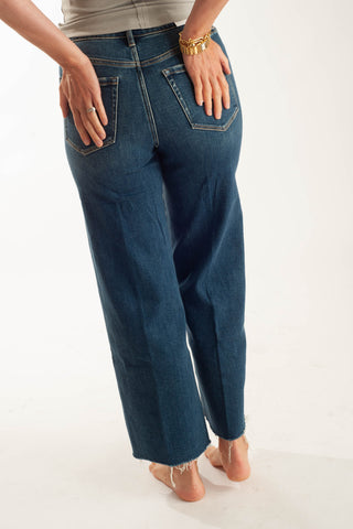 A person shown from the back wearing dark blue wide-leg jeans, standing barefoot against a plain white studio background.