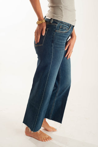A person wearing dark blue wide-leg cropped jeans with a frayed hem, paired with a light gray top, shown from the waist down against a plain white studio background.
