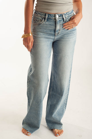 A person wearing light-wash blue wide-leg jeans, shown from the waist down against a plain white studio background.