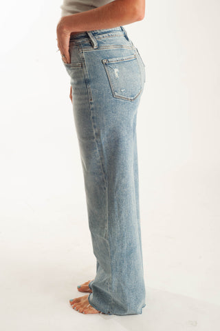 A person shown from the waist down wearing light-wash blue wide-leg jeans, standing barefoot against a plain white studio background.