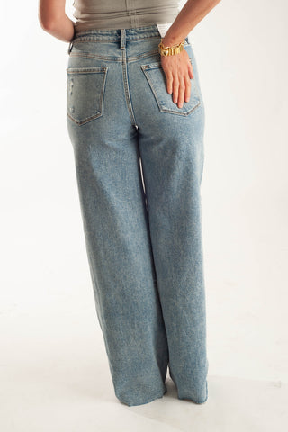 A person shown from the back wearing light-wash blue wide-leg jeans, standing against a plain white studio background.