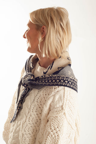 A woman in profile wearing a cream cable-knit sweater and a navy blue patterned scarf tied around her neck, photographed against a clean white background.