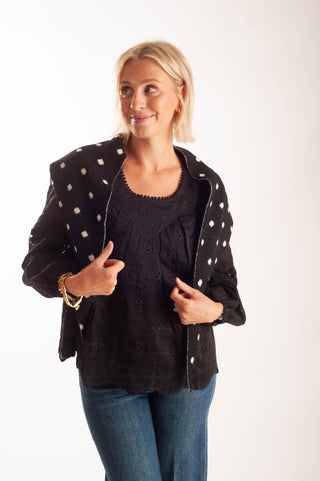 A woman modeling a black textured jacket with white polka dots over a black top and blue jeans, photographed against a plain white studio background.