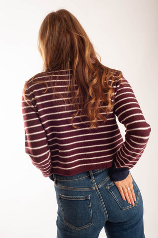 A woman viewed from behind wearing a burgundy and cream striped knit sweater and blue jeans against a plain white background.