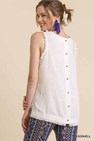 Woman wearing a white sleeveless top with buttons and patterned pants on a beige background