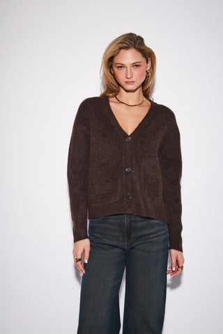 A woman modeling a dark brown fuzzy knit cardigan with a V-neck and button closure, paired with dark blue jeans, against a plain light gray background.