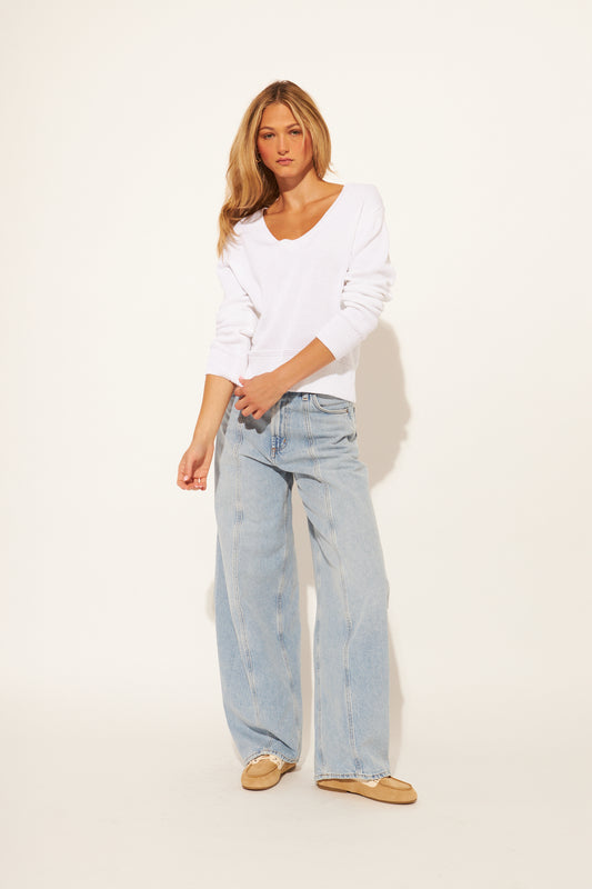 Woman wearing a white sweater and light blue jeans on a plain background