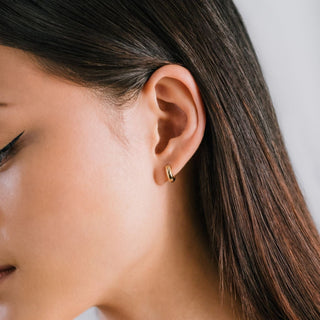 Close-up of a woman wearing a gold earring with a neutral background