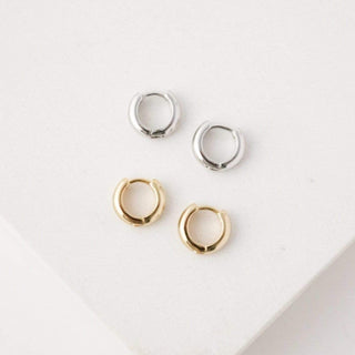 a pair of silver and gold hoop earrings laying on a table