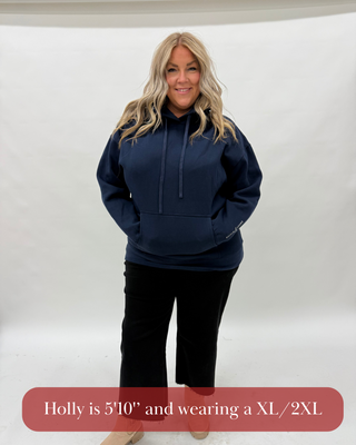 Woman wearing a navy hoodie and black pants on a white background