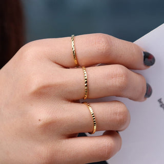 A person's hand showcasing three gold-colored rings on the fingers. The rings appear to have a textured finish.