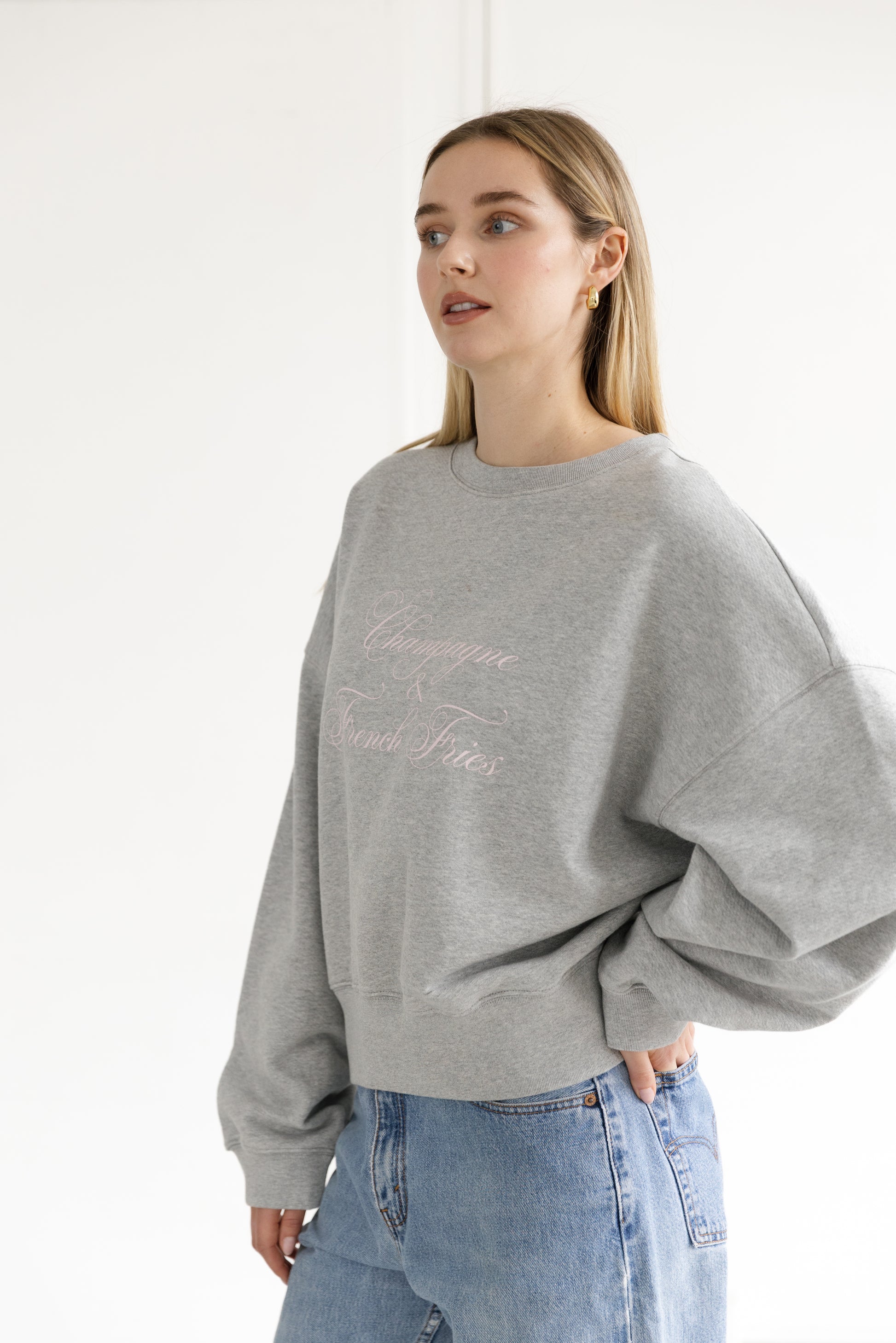 Woman wearing a gray sweatshirt with text and blue jeans on a white background