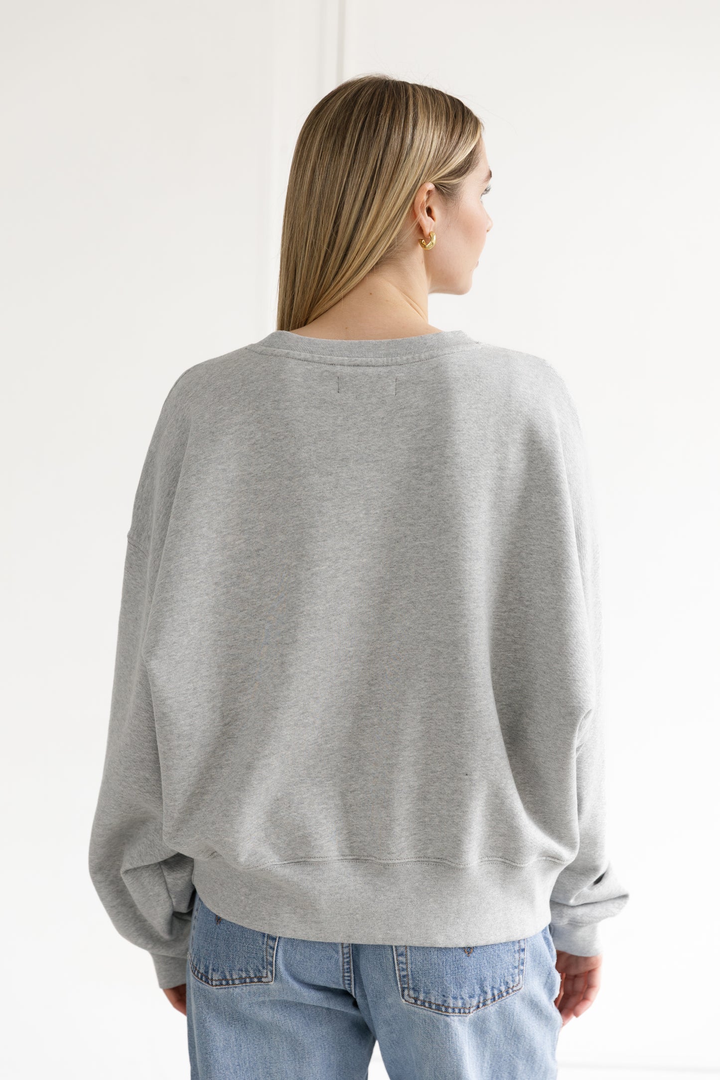 Person wearing a gray sweater and light blue jeans against a white background