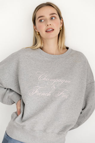 Woman wearing a gray sweatshirt with 'Champagne & French fries' text on a white background