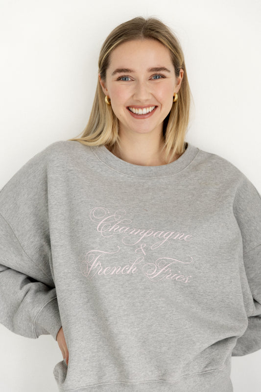 Woman wearing a gray sweatshirt with 'Champagne & French Fries' text on a white background