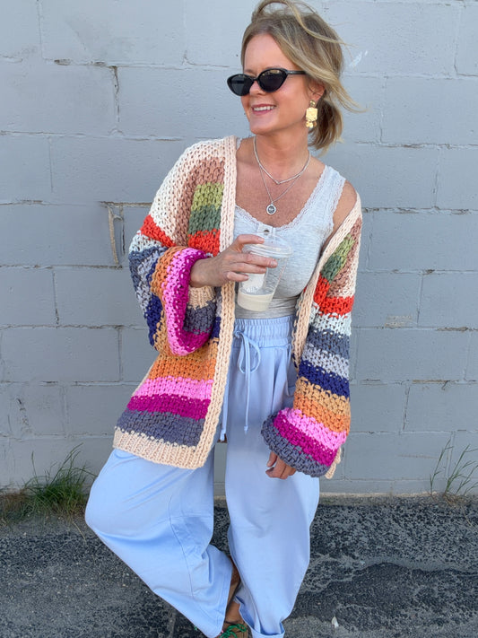 Woman wearing a colorful striped cardigan against a gray wall.
