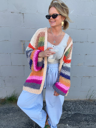 Woman wearing a colorful striped cardigan against a gray wall.