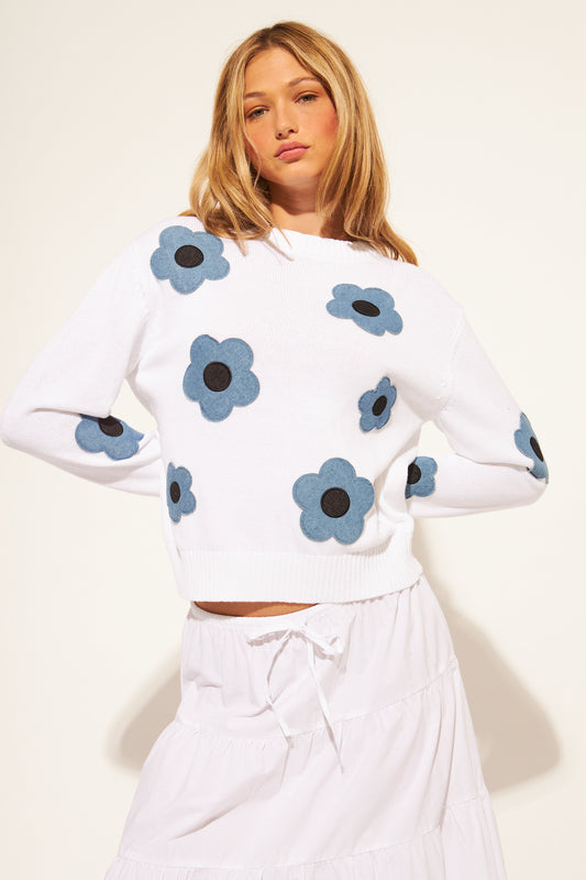 Woman wearing a white sweater with blue floral patterns on a plain background