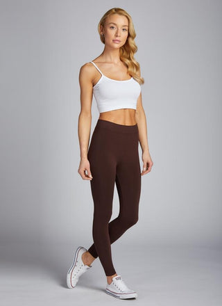 A woman wearing a white crop top and dark full-length leggings, standing against a plain background.