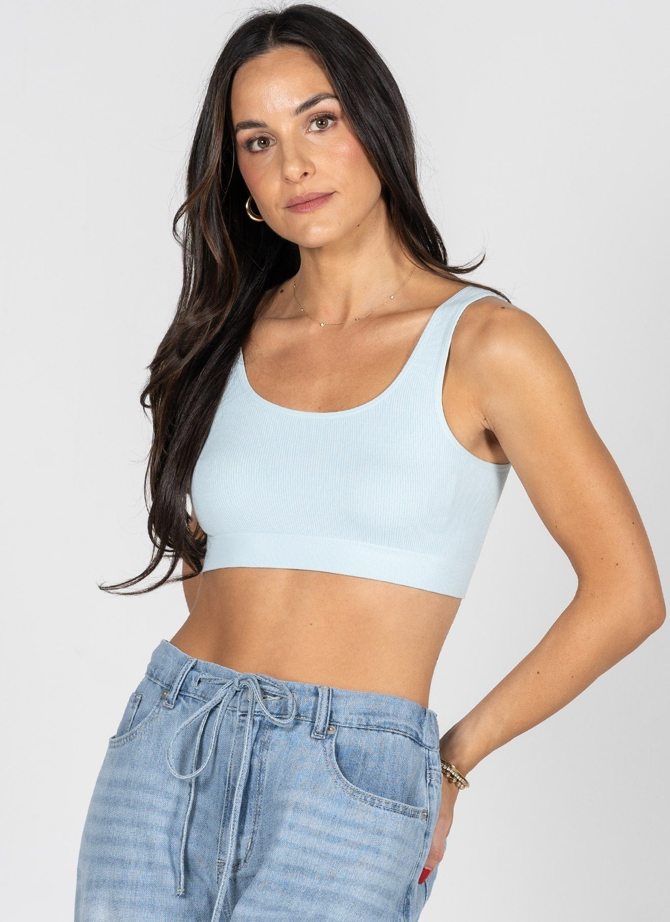 Woman wearing a light blue sports bra and jeans on a plain background