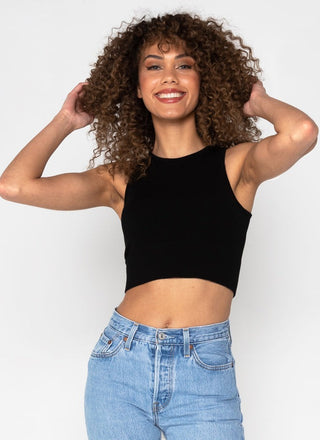 A woman wearing a white high neck crop tank top and blue jeans.