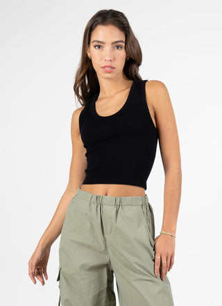 A person wearing a black ribbed bamboo fabric tank top with a deep scoop neck and short sleeves, paired with green cargo pants.