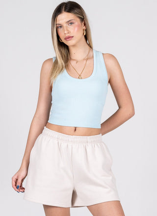 Woman wearing a light blue tank top and beige shorts on a white background