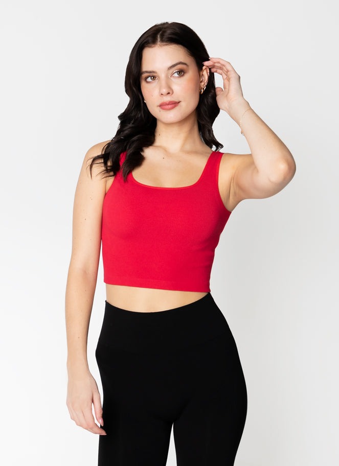 Woman wearing a red tank top and black leggings on a white background
