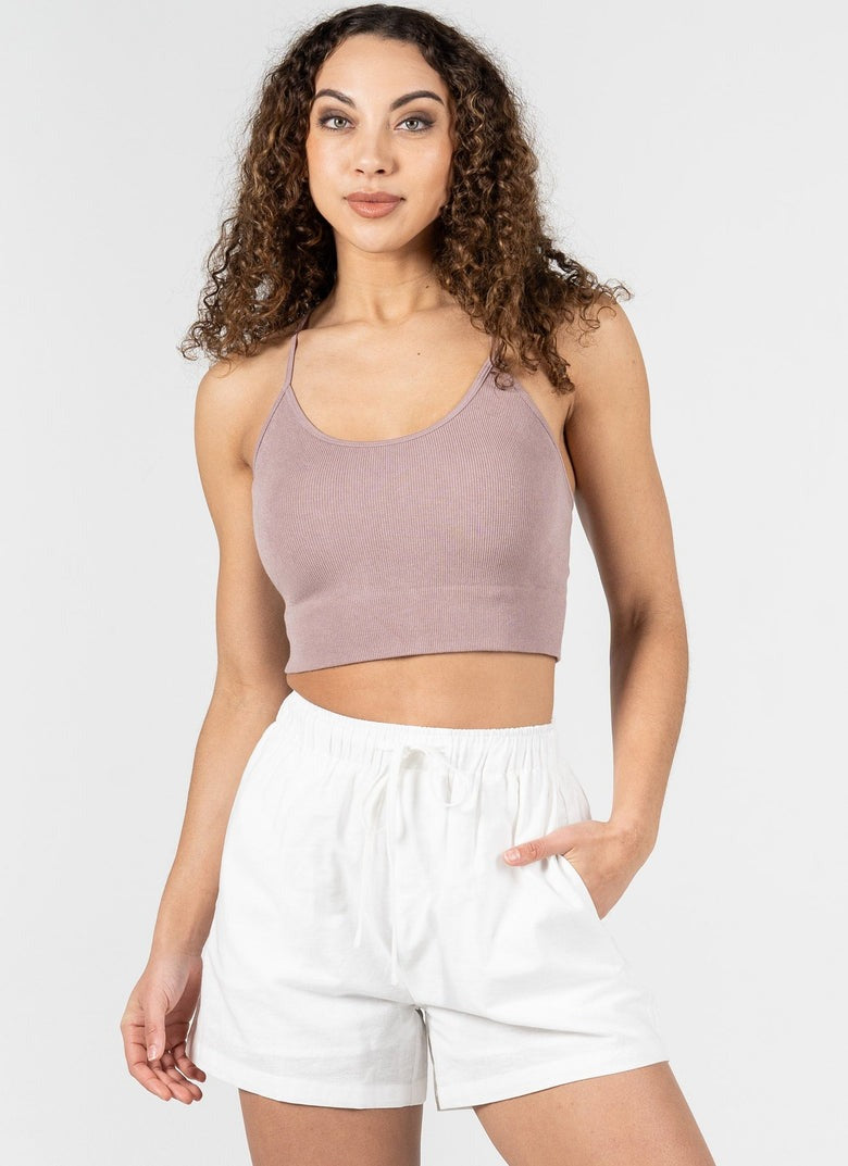 Woman wearing a mauve tank top and white shorts on a plain background