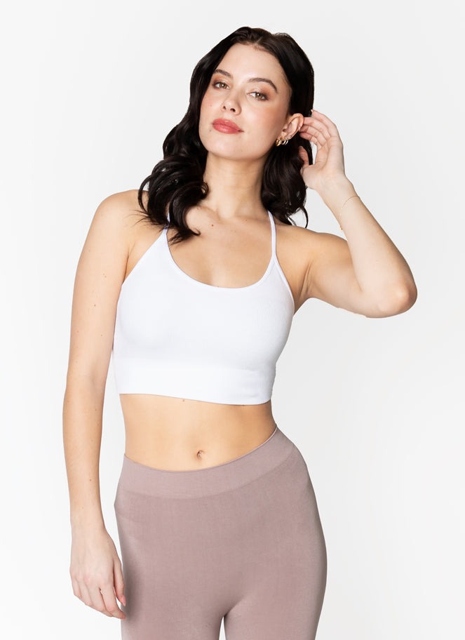 Woman wearing a white sports bra and brown leggings on a plain background