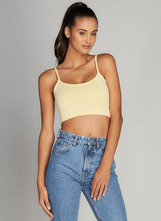 Woman wearing a yellow tank top and blue jeans against a gray background