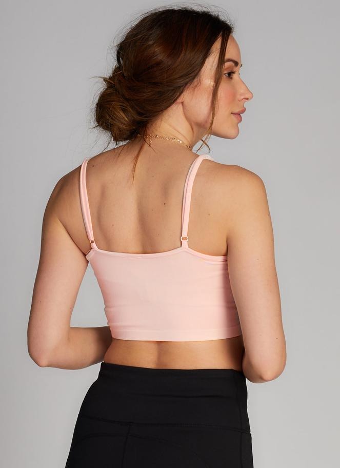 Woman wearing a light pink sports bra and black leggings against a gray background