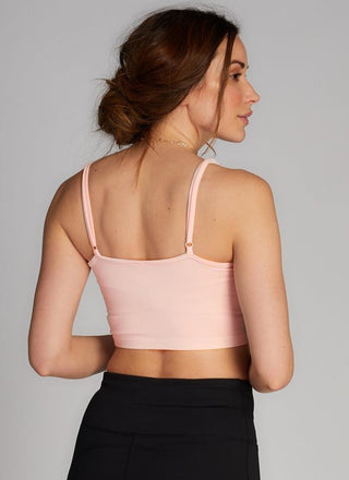Woman wearing a light pink sports bra and black leggings against a gray background