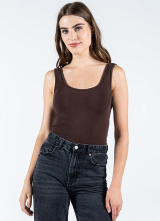 Woman wearing a brown tank top and black jeans on a white background