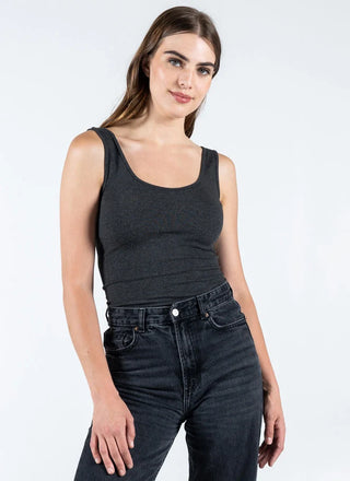 Woman wearing a black tank top and dark jeans on a white background