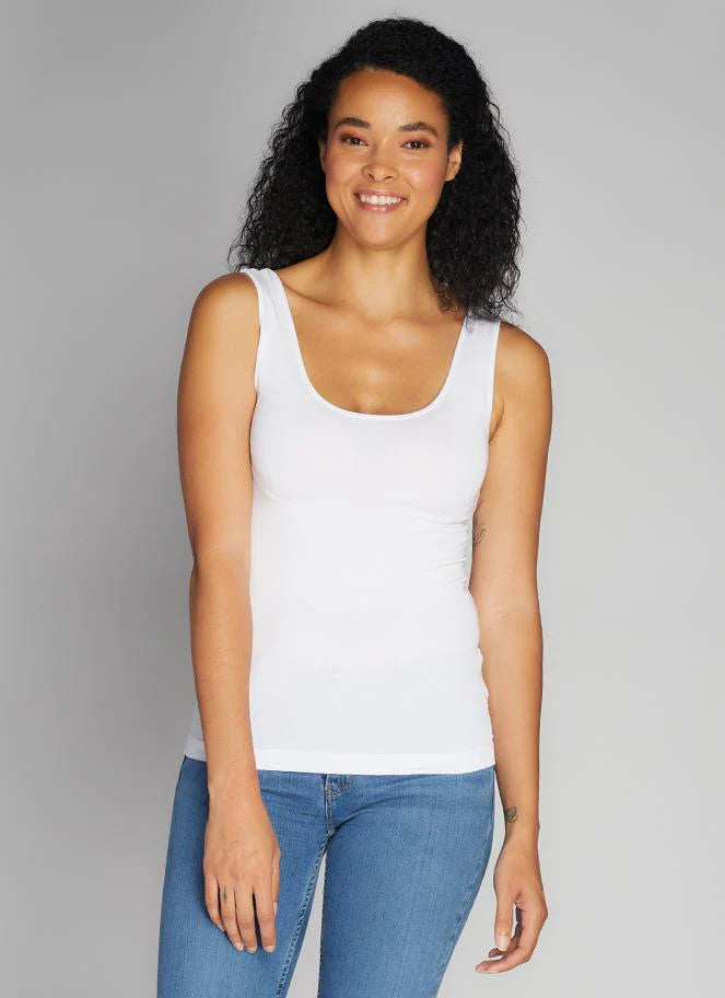 Woman wearing a white tank top and blue jeans against a gray background