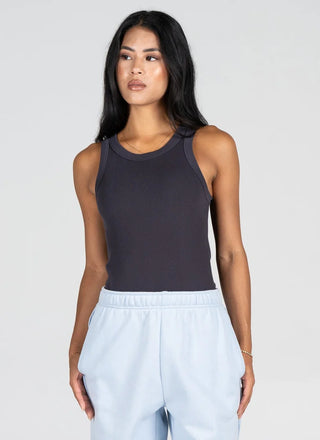 A woman modeling a dark charcoal gray ribbed sleeveless tank top paired with light blue sweatpants, set against a plain light gray studio background.