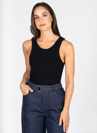 A woman modeling a black ribbed tank top paired with dark blue jeans against a plain light gray studio background.
