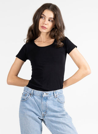 A woman wearing a short sleeve scoop neck top in black with jeans. 