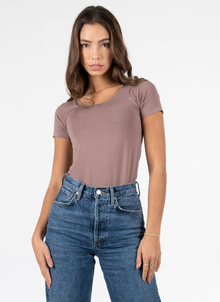A woman wearing a short sleeve scoop neck top in taupe with jeans. 