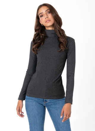 Woman wearing a dark gray turtleneck sweater and blue jeans on a white background