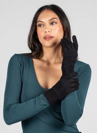 A woman wearing a dark teal long-sleeve top and black knit gloves, posing against a light gray studio background.