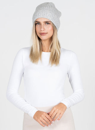 Woman wearing a white long-sleeve top and gray beanie against a plain background