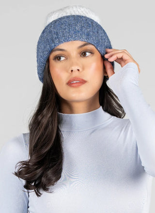 A woman wearing a blue and white knit beanie hat and a light blue mock-neck top, posing against a solid light gray background.