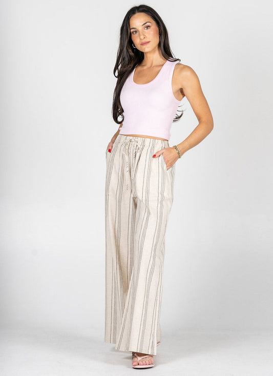 Woman wearing a light pink sleeveless top and beige striped pants on a white background